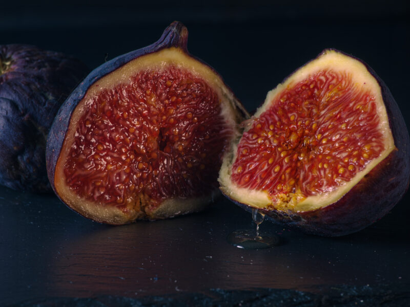 Aufgeschnittene Feige mit tropfendem Saft auf dunkler Steinplatte, Dark & Moody Foodfotografie