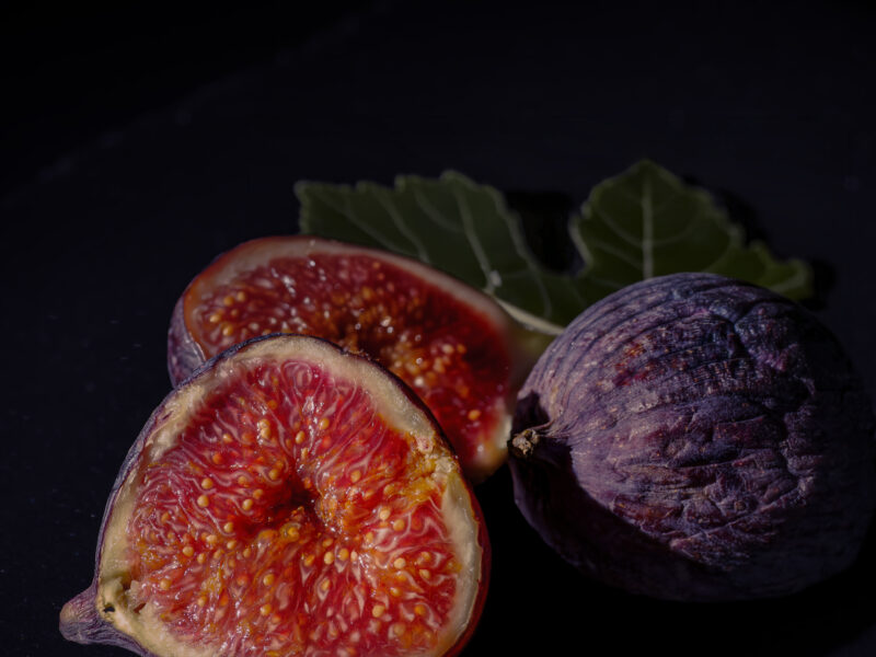 Halbierte Feige mit Feigenblatt vor dunklem Hintergrund, dramatisches Licht, Dark & Moody Foodfotografie